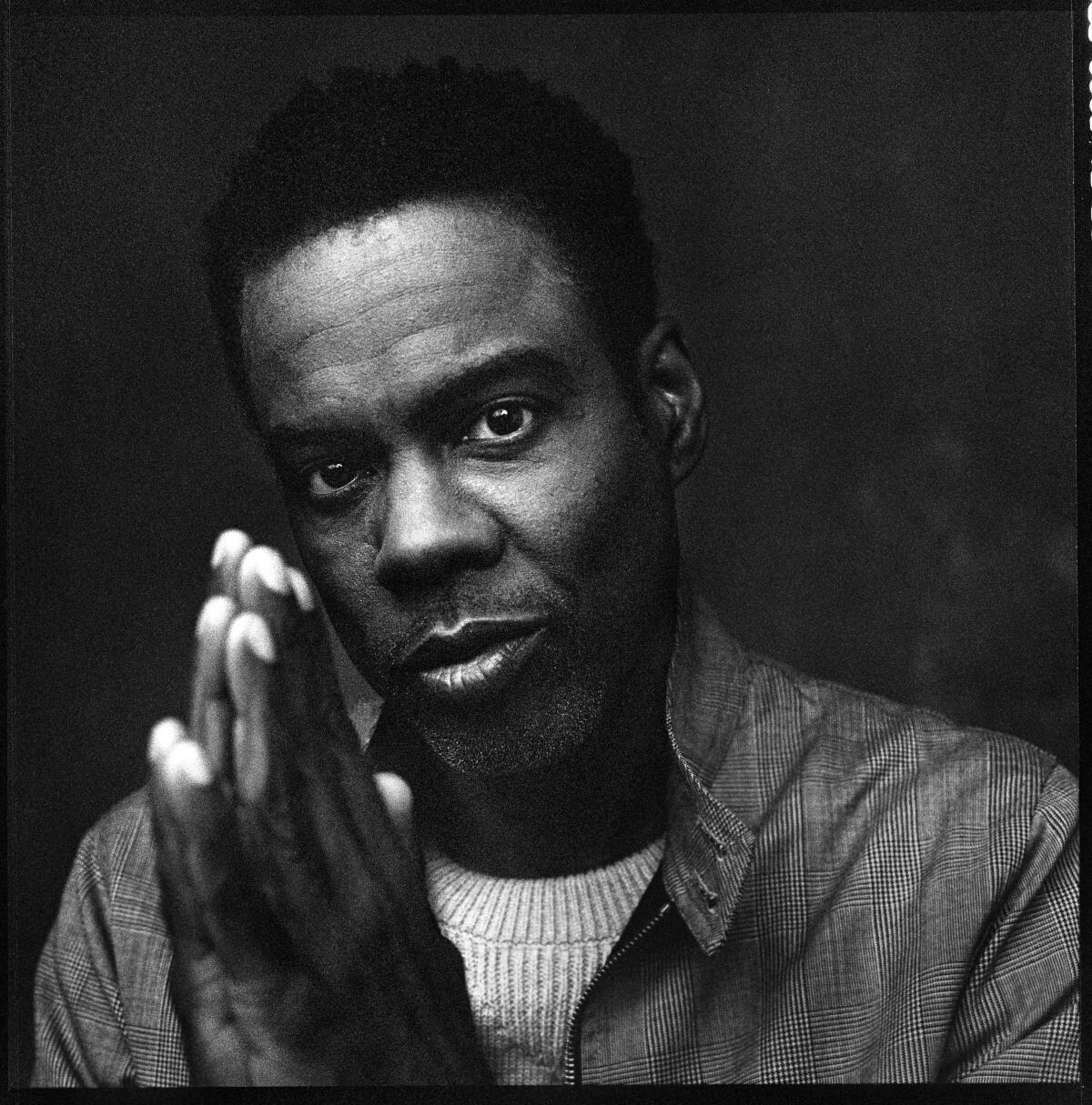 Chris Rock, in a black-and-white photo, holds up his hands as if in prayer