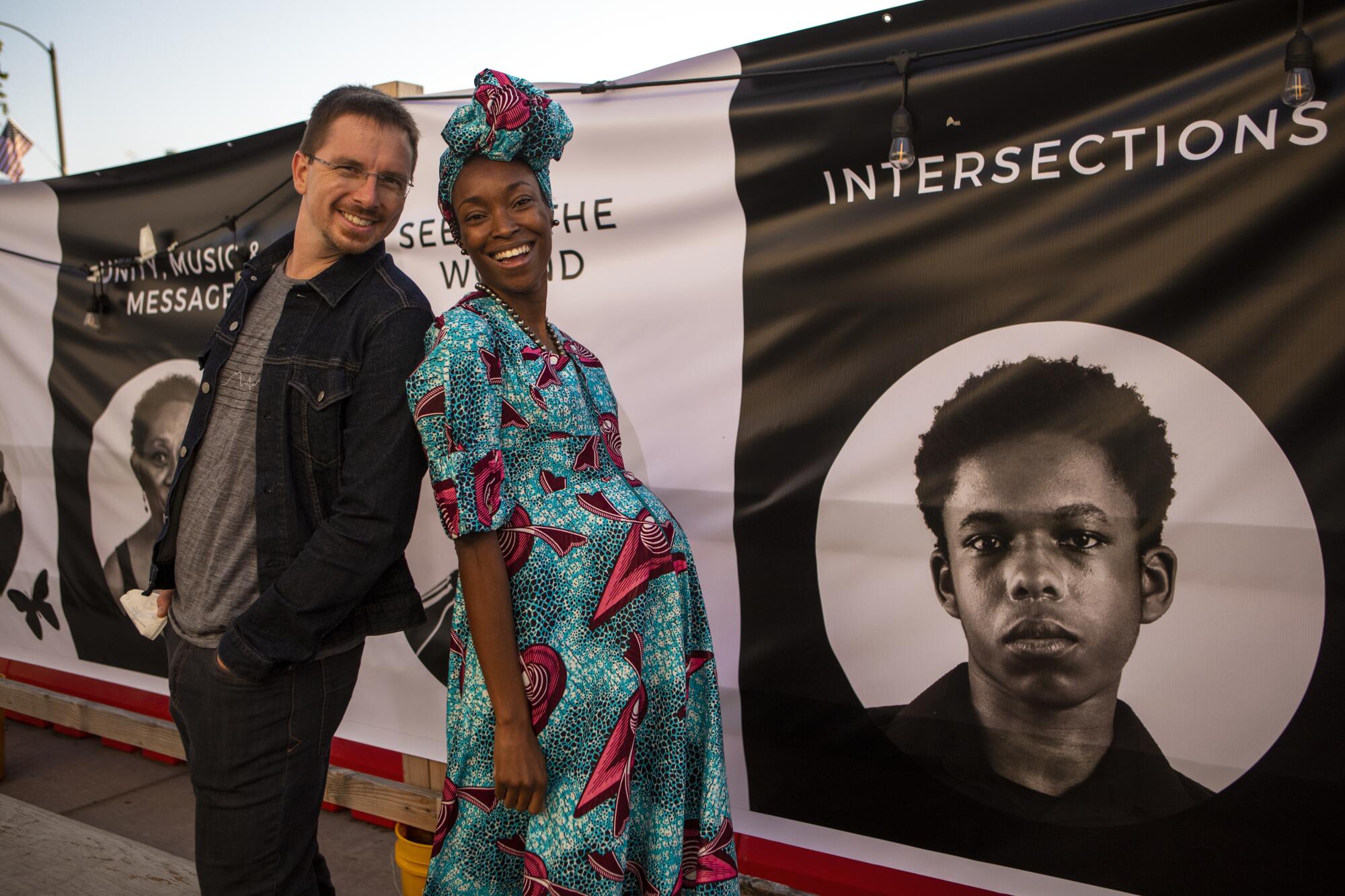 A man and woman smile as they stand in front of a banner featuring Black faces