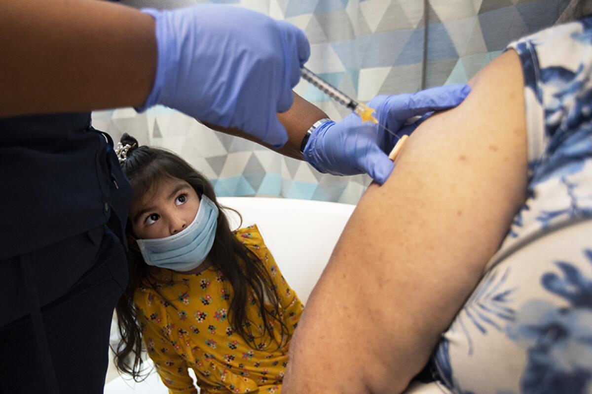 A young girl watches her grandparent get vaccinated. 