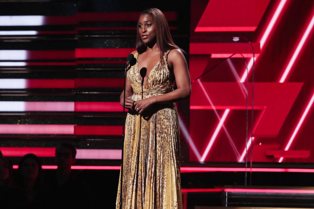 A woman in evening attire stands on stage in front of a microphone