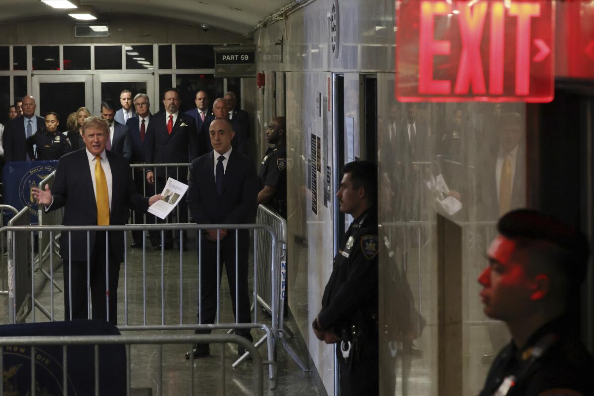 Former President Trump stands behind a metal barrier, speaking and gesturing.