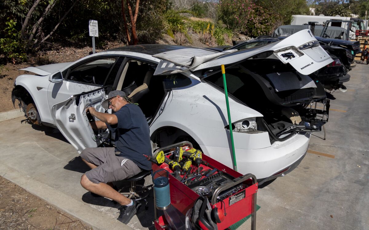 A worker removes parts from a totaled Tesla to use in converting gas-powered vehicles to electric.