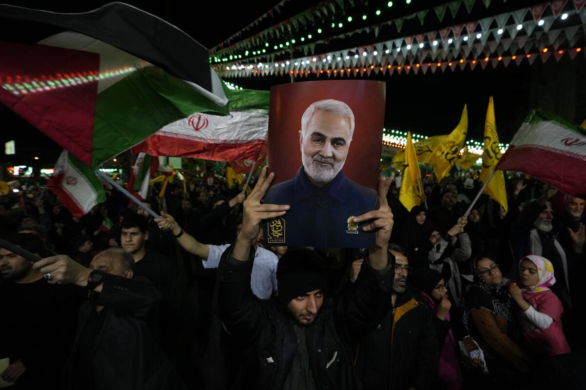 Iranian protesters wave Iranian and Palestinian flags. One person holds up a poster of the late Gen. Qassem Soleimani.