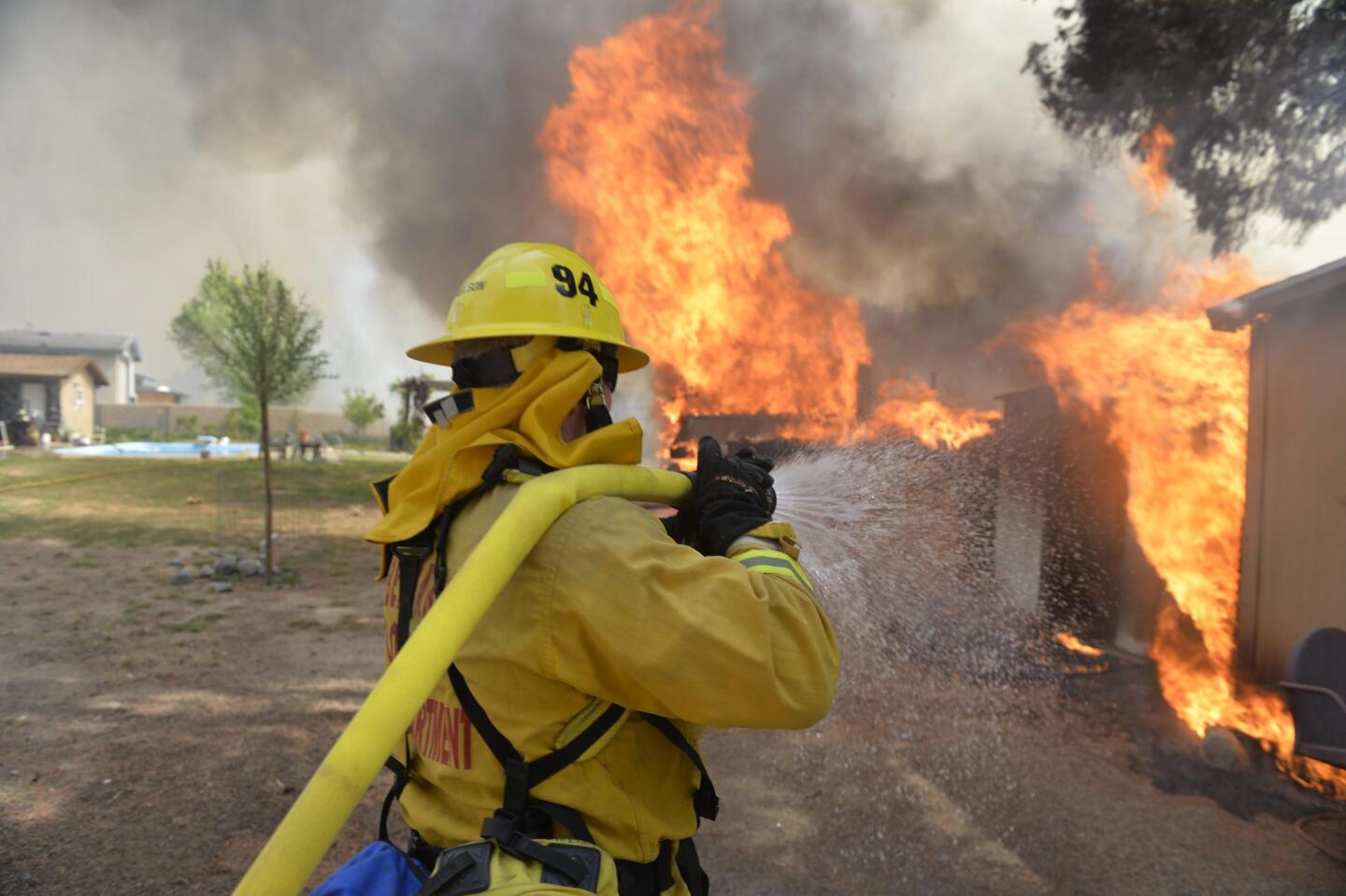 A firefighter battling the River Bottom fire sprays water on burning buildings near Hesperia and Apple Valley in San Bernardino County on March 31.