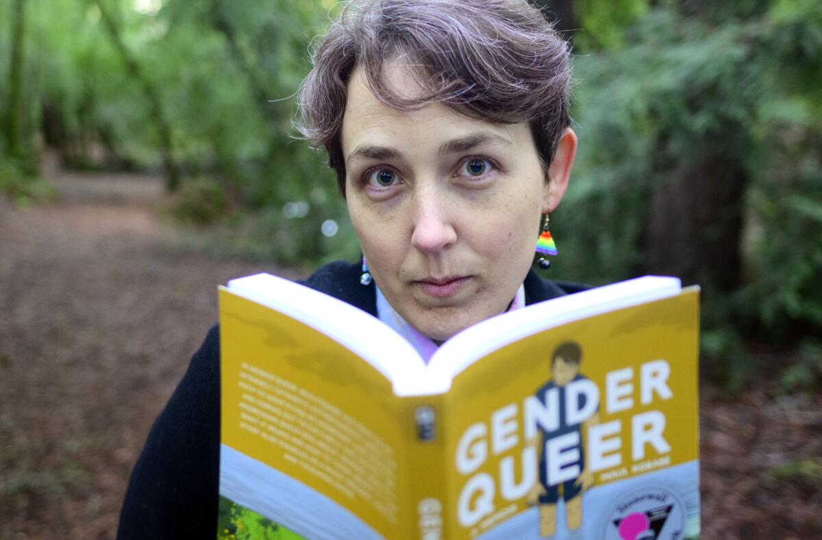 A person standing in a park holds up a graphic novel with the title "Gender Queer"