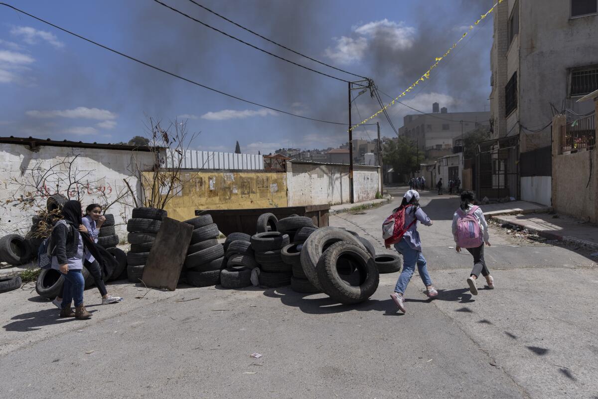 Palestinian students walk past piles of tires.