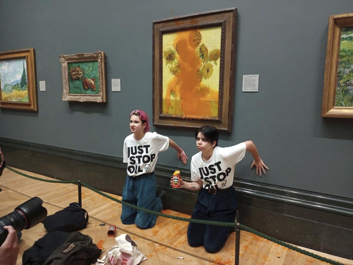 Two protesters kneel in front of a painting covered in tomato soup.