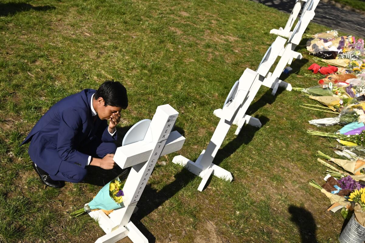 A mourner prays at a makeshift memorial featuring white crosses 