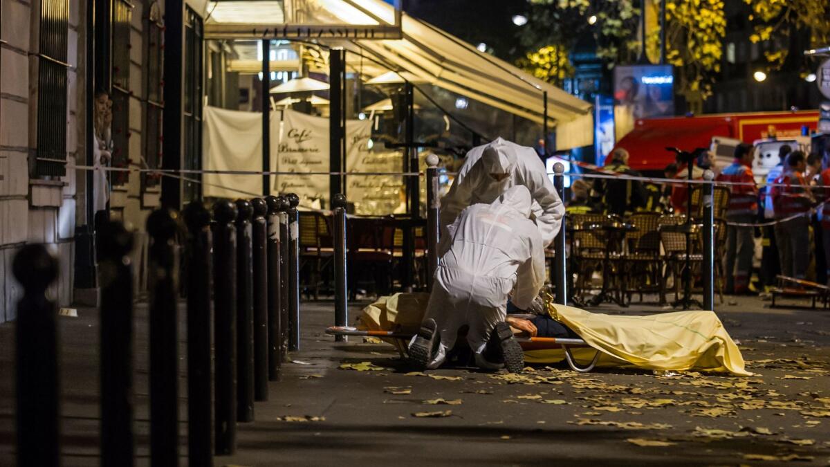 Investigating police officers inspect the lifeless body of a victim of a shooting attack outside the Bataclan concert hall in Paris on Nov. 13, 2015. (Kamil Zihnioglu / Associated Press)