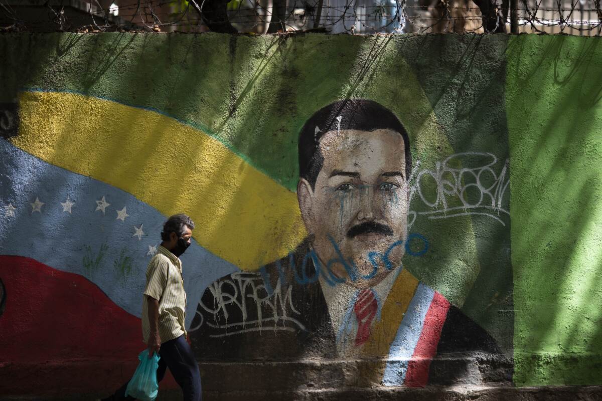 A man wearing a face mask amid the COVID-19 pandemic passes a mural of Venezuelan President Nicolas Maduro in Caracas, Venezuela, Wednesday, July 22, 2020. Analysts say that in recent months the pandemic has helped suck away the opposition’s scanty momentum and bolster Maduro’s already strong hand. (AP Photo/Ariana Cubillos)