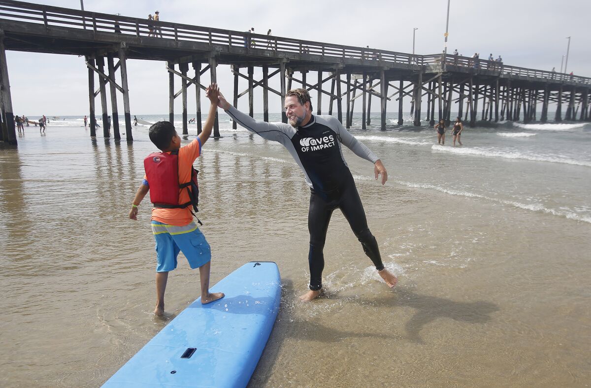 Kenneth Avendano and instructor Joe Iredell high-five each other after a ride in the waves during the Miracles for Kids surf camp at the Newport Pier on Friday.