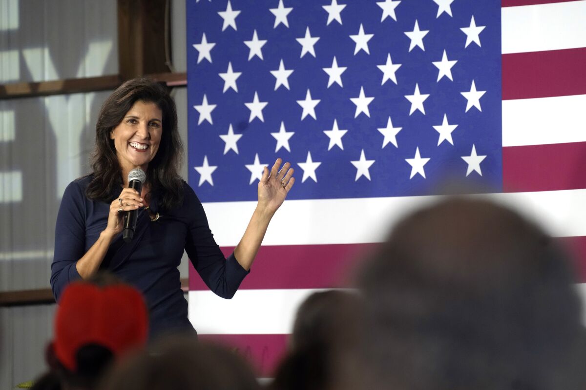 Nikki Haley holding a microphone on stage in front of an American flag