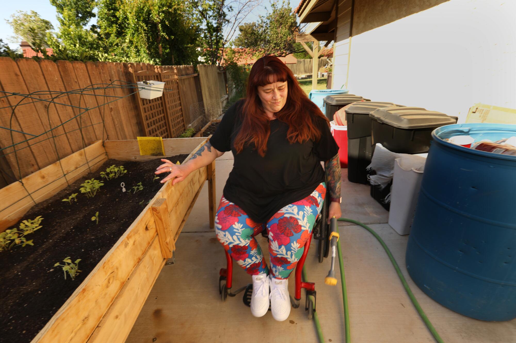 A woman in a wheelchair tugs at a garden hose in a home's side yard
