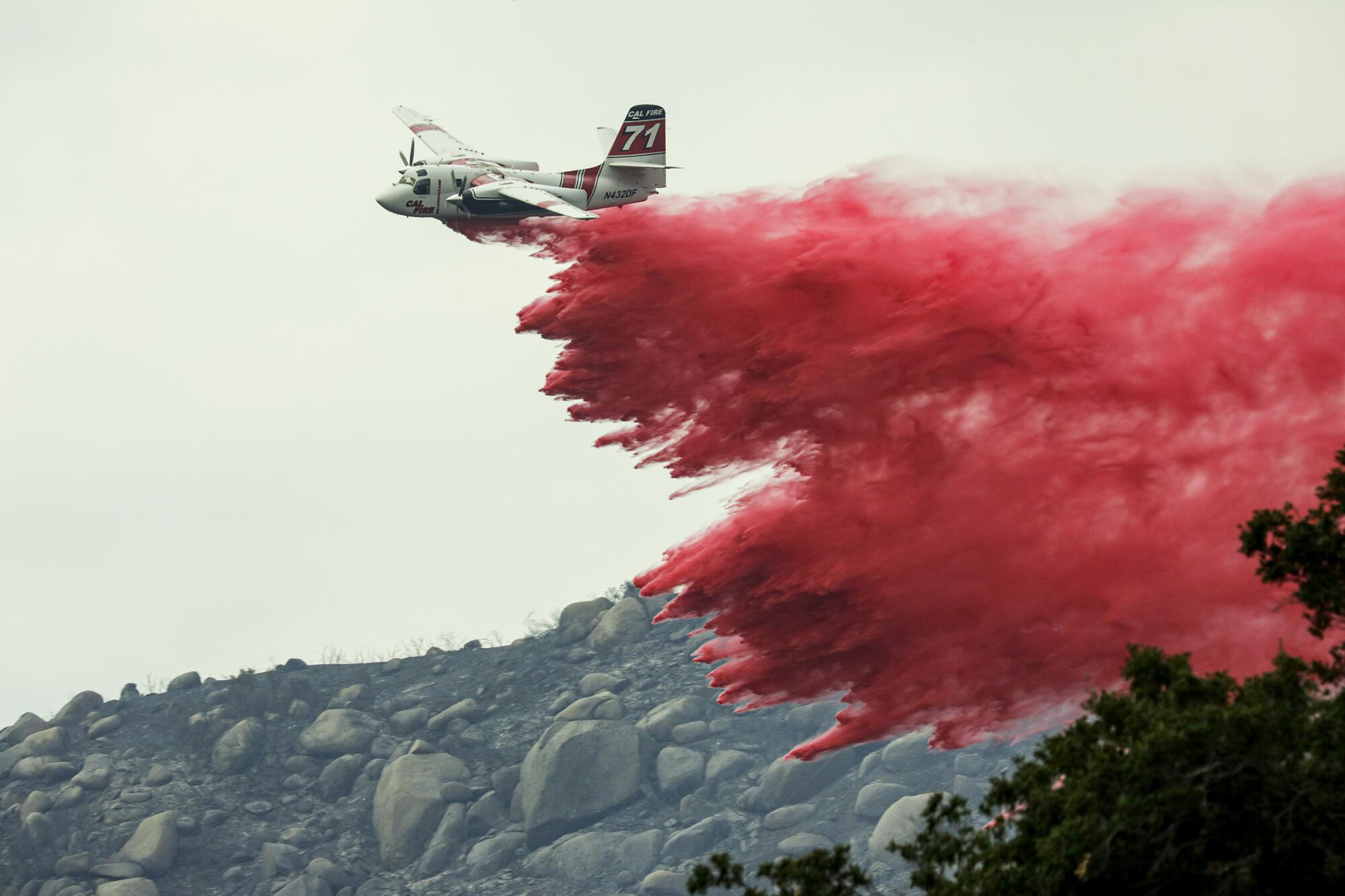 A plane drops fire retardant on a brush fire burning on a rocky hillside.  