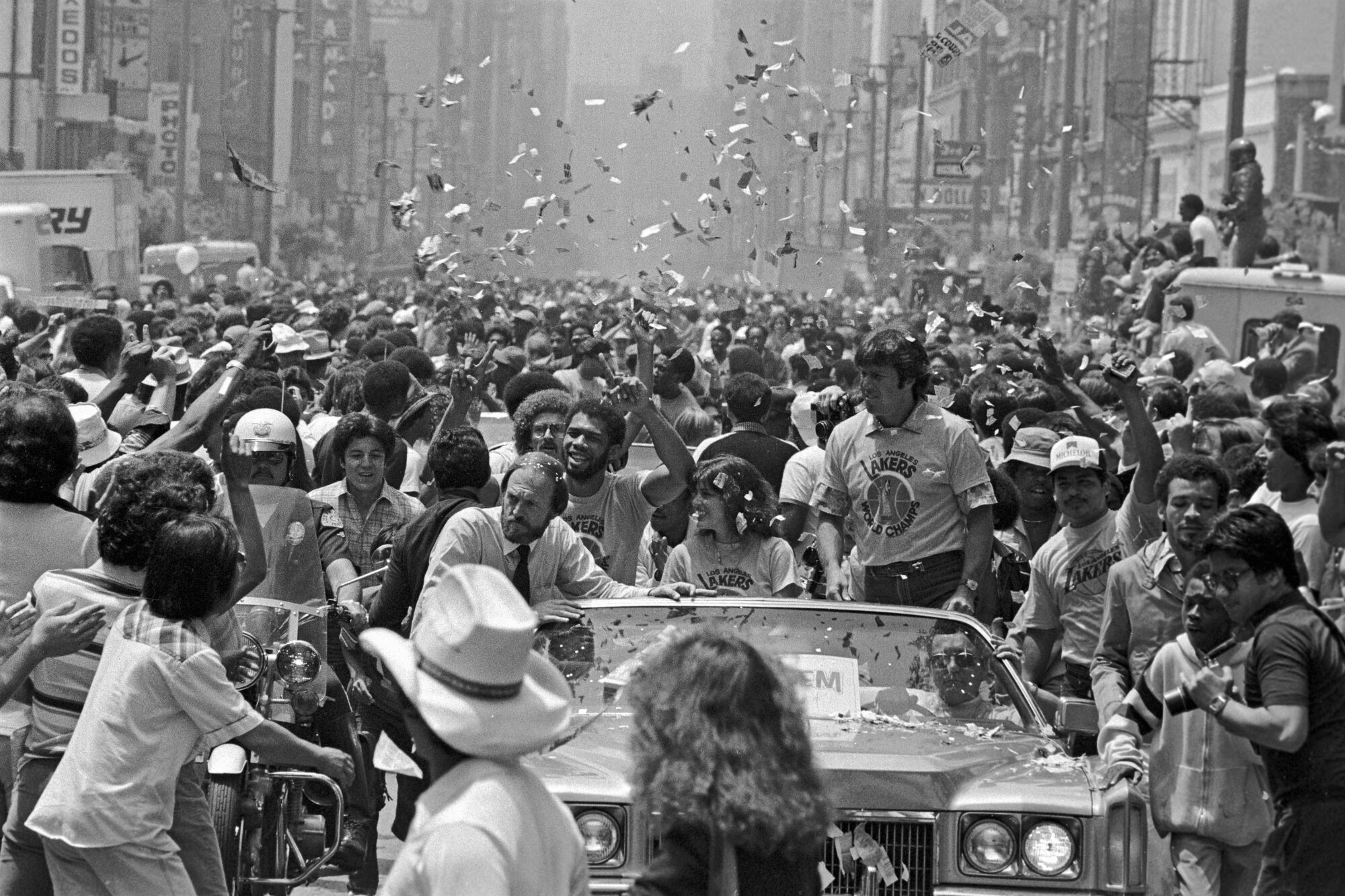 Kareem Abdul-Jabbar, sitting in a convertible and surrounded by crowds, holds up his finger in a gesture of number one.