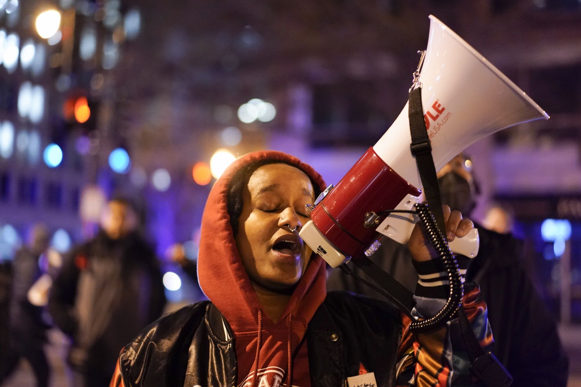 A person closing their eyes while using a megaphone, with city lights in the background