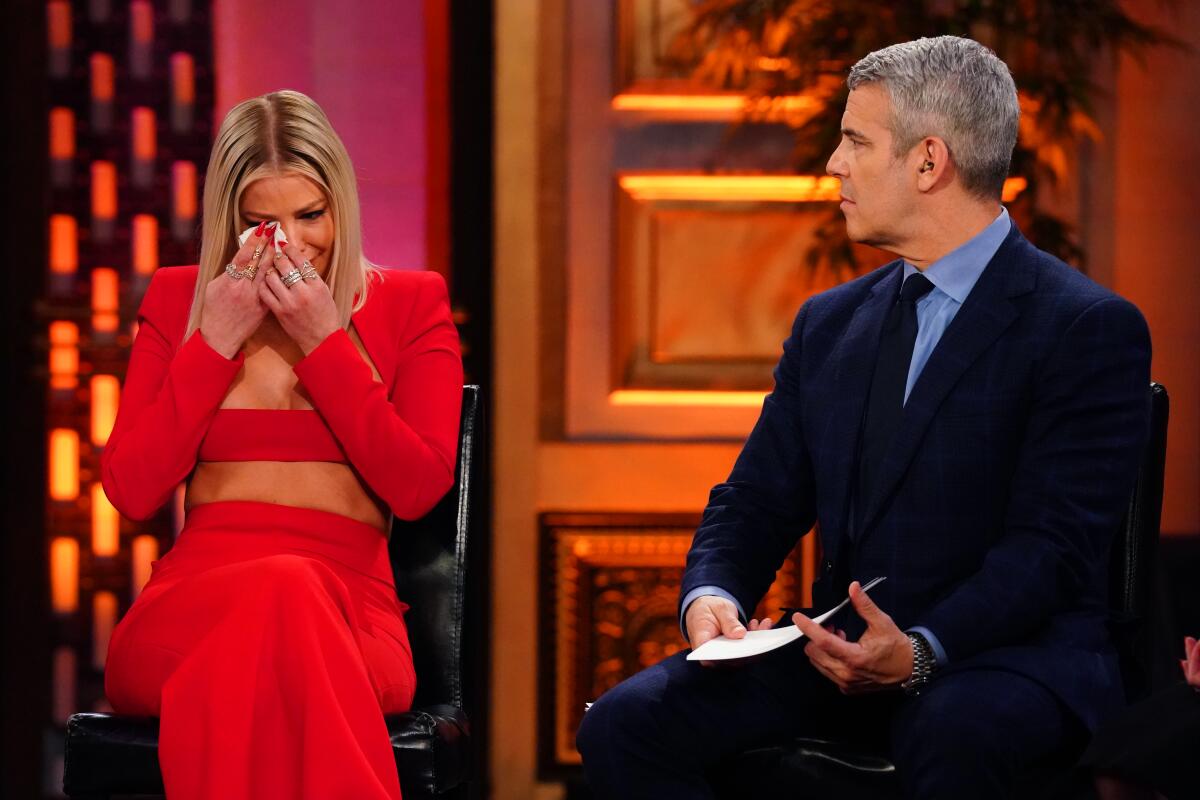 A woman in a red dress cries while a man in a suit looks on.