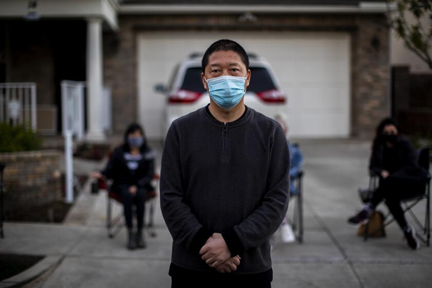 MISSION VIEJO, CA - FEBRUARY 25, 2021: Haijun Si stands in front of his Ladera Ranch family home as neighbors gather in front to form a nightly security detail after local teens have harassed the family by throwing rocks and yelling racial slurs on February 25, 2021 in Mission Viejo, California.(Gina Ferazzi / Los Angeles Times)