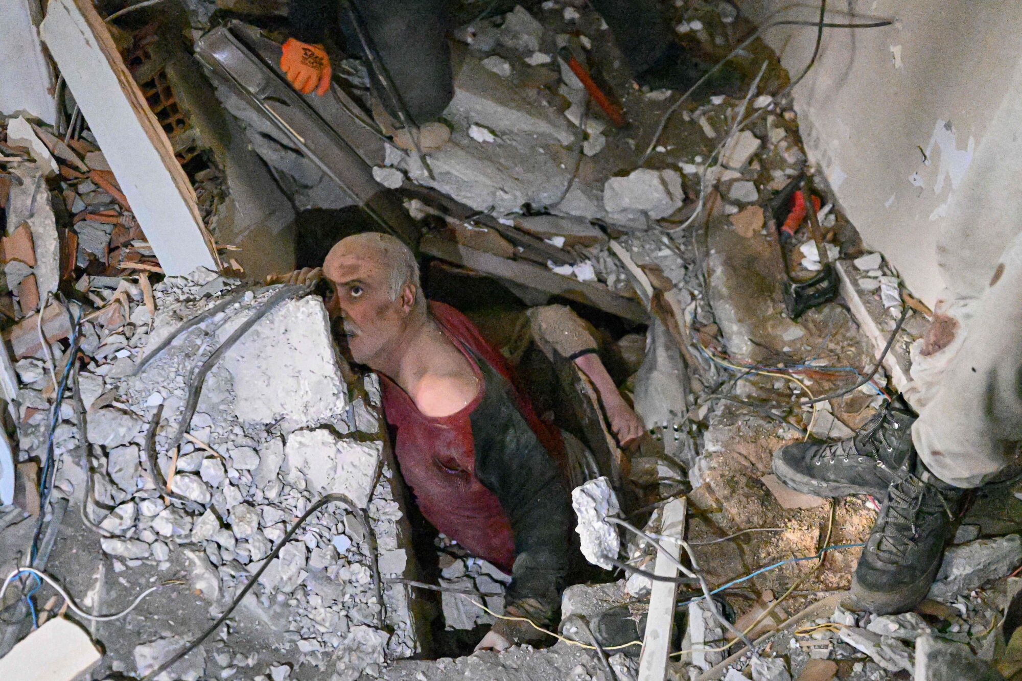 A man watches his rescuers remove debris from the destroyed building where he was trapped in Hatay, Turkey