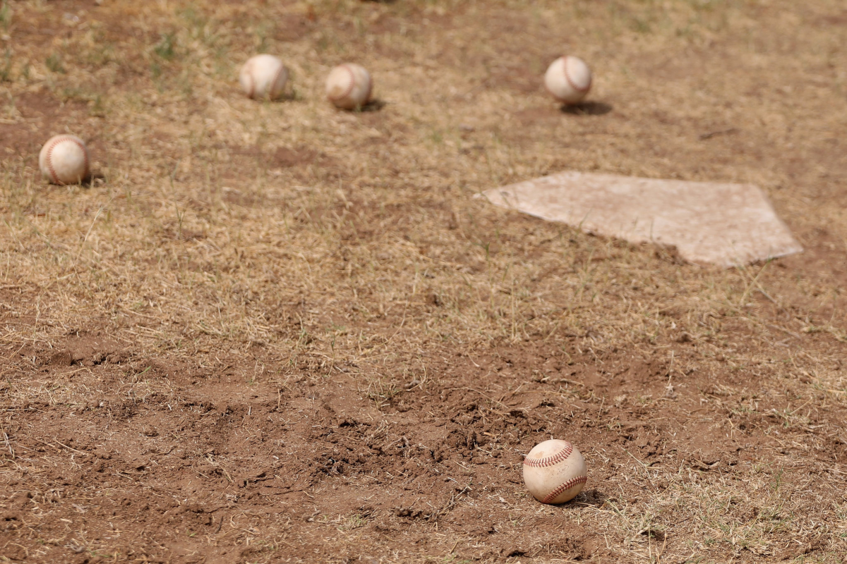 Five baseballs lie in the dirt near home plate.