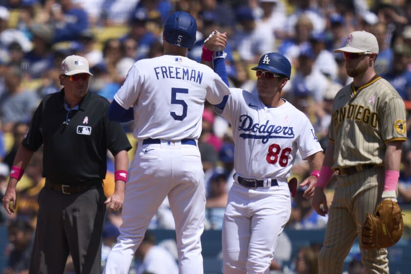 Los Angeles Dodgers' Freddie Freeman (5) high-fives first base coach Clayton McCullough after hitting a single during the sixth inning of a baseball game against the San Diego Padres, Sunday, May 14, 2023, in Los Angeles. (AP Photo/Allison Dinner)