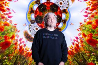 Artist Chris Holmes wears a navy sweatshirt and stands before his colorful kaleidoscopic art piece "The Journey Within."  