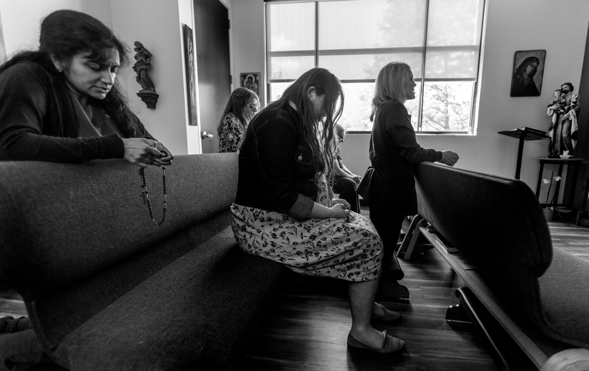 Women sit on pews and kneel to pray in a chapel