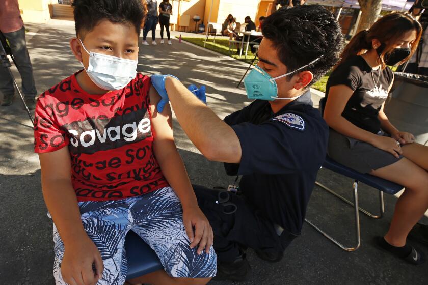 ARLETA, CA - AUGUST 02: 12-year-old Alessandro Roque, receives his Pfizer Covid vaccine from Brandon Jaramillo, an EMT with FirstMed Ambulance Services as the Fernandeno Tataviam Band of Mission Indians, in its participation with the Medi-Vaxx Program of the San Fernando Valley, along with El Proyecto del Barrio, Los Angeles Mission College, Mission Hospital and FirstMed Ambulance Services conducted one in a series of pop-up COVID-19 vaccination clinics at Montague Charter Academy for the Arts and Sciences in Arleta Monday morning. Monday's clinic administered first doses of the Pfizer and J&J vaccine and ran through noon. Montague Charter Academy for the Arts and Sciences on Monday, Aug. 2, 2021 in Arleta, CA. (Al Seib / Los Angeles Times).