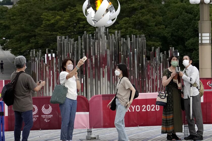 TOKYO, - JULY 30: People take selfies in front of the Olympic Cauldron. Below them a small homeless camp is located under the Tokyo Olympic Cauldron.Tokyo Olympics on Friday, July 30, 2021 in Tokyo, {stmens}. (Gary Ambrose / For the Times)