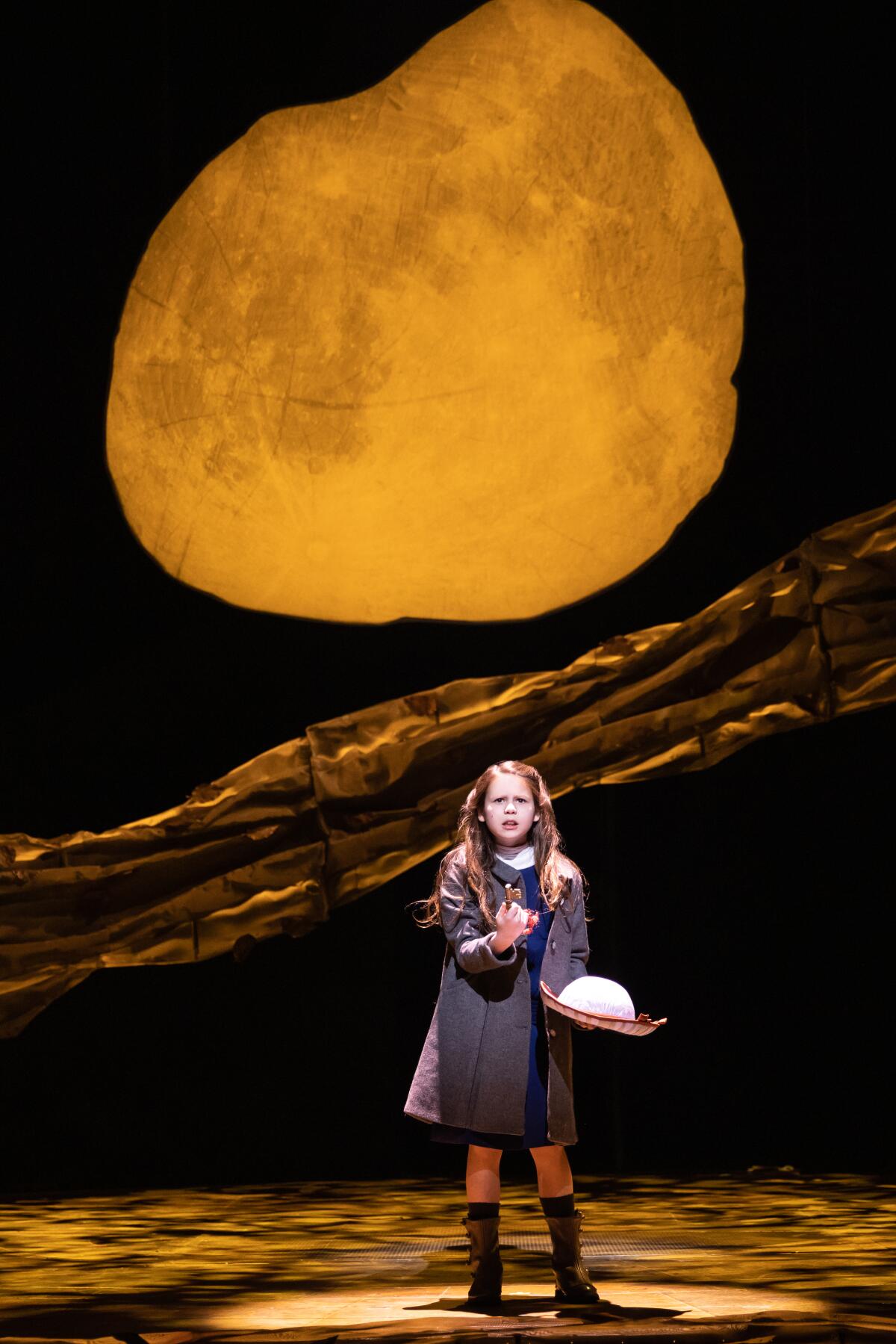 A young actor on a stage with a full moon behind her.