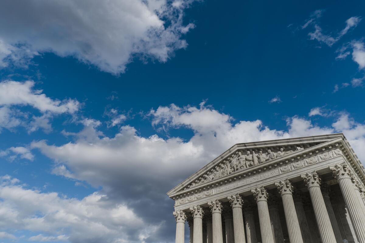A view of the U.S. Supreme Court building with blue skies and light clouds in the background.