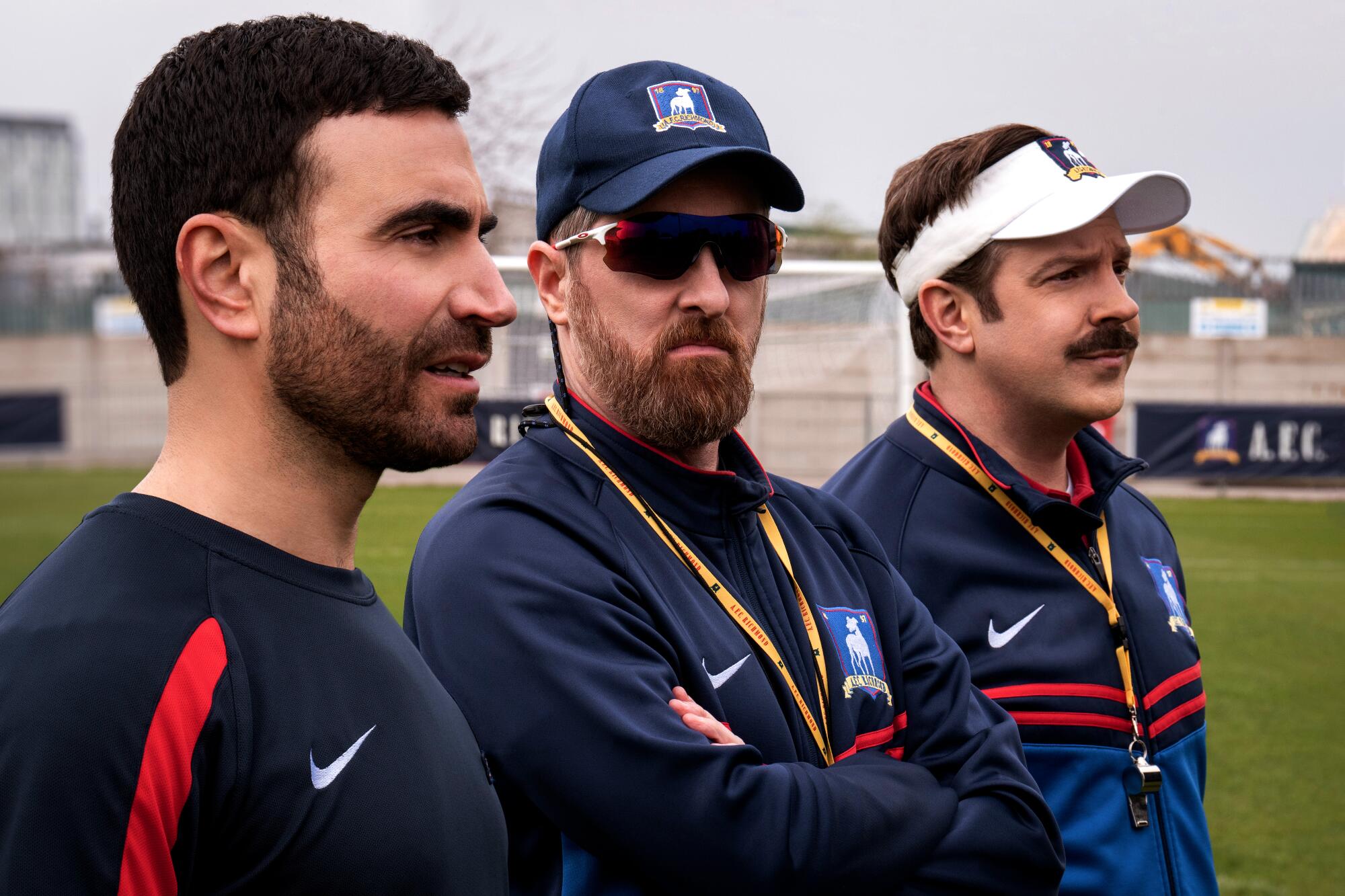 Three football coaches look out onto the pitch