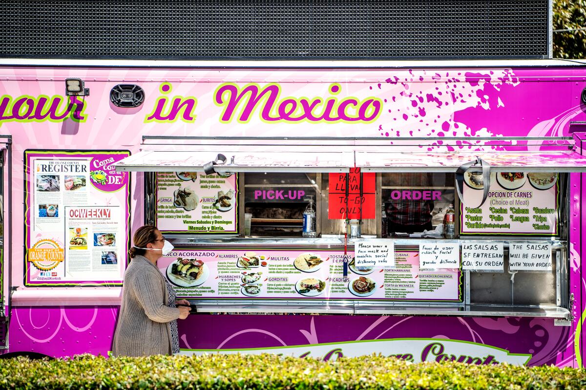 A customer wearing a mask places an order at Alebrijes taco truck on Wednesday, April 22, 2020 in Santa Ana.