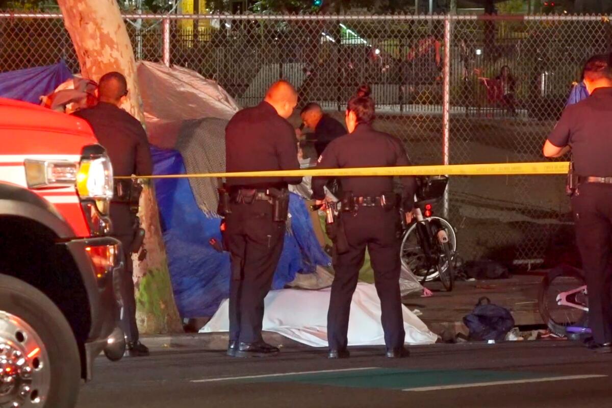 Police officers stand near a sidewalk next to a body covered by a sheet
