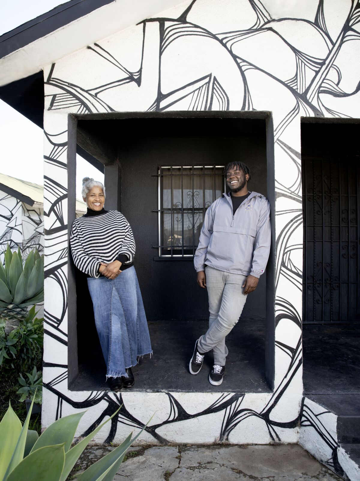 Janine Watkins and Demar Matthews are framed by porch columns in a house painted with a swirling black and white design.