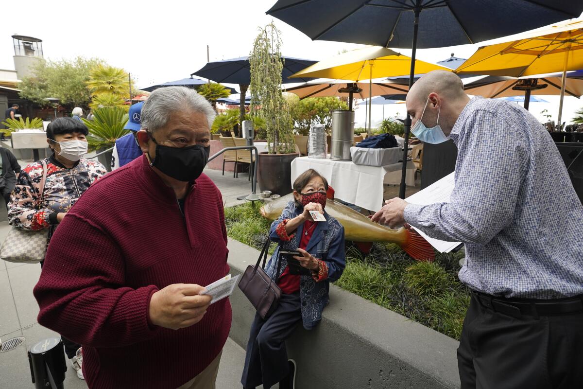 FILE - In this Aug. 20, 2021, file photo, host Jason Pryor, right, checks the vaccination and identification cards of diners as they enter the Waterbar restaurant in San Francisco. Indoor masking requirements in the San Francisco Bay Area will be eased for certain indoor public settings, including offices, gyms, college classrooms and churches, once counties reach low COVID-19 case and hospitalization rates and at least 80% of the total population is fully vaccinated, officials announced Thursday, Oct. 7, 2021. (AP Photo/Eric Risberg, File)