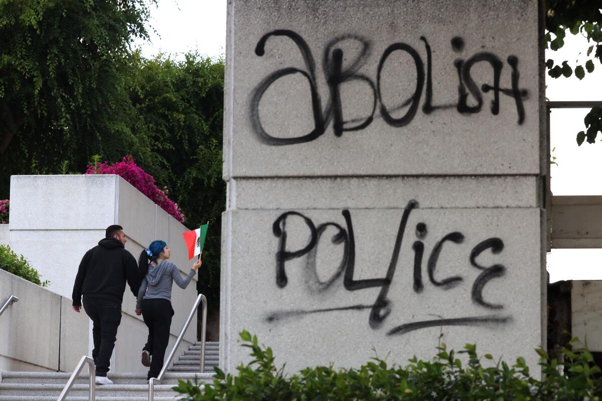 A pair of immigrant rights activists walk past graffiti while joining a protest against federal immigration authorities.