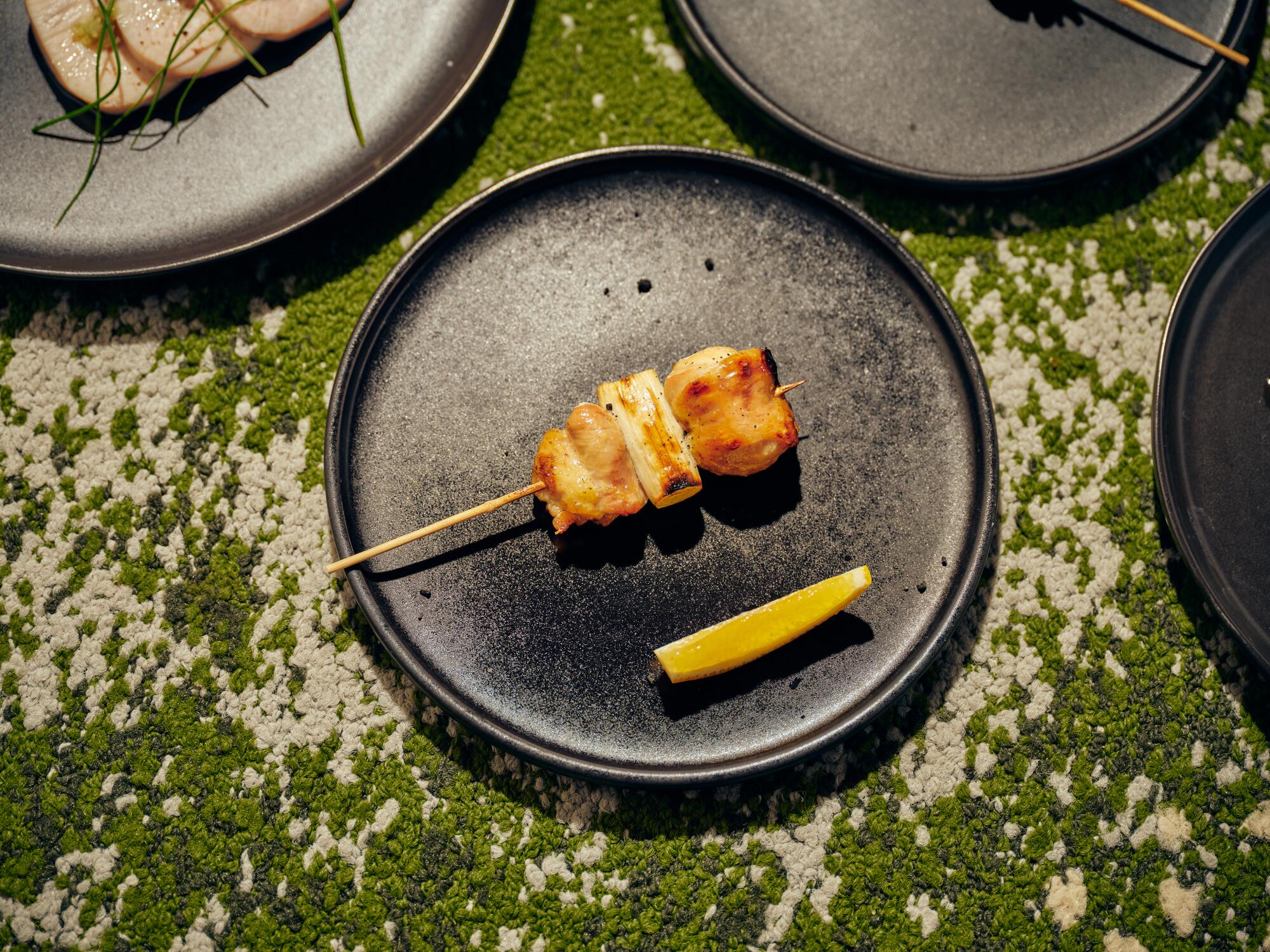 A single chicken oyster negima skewer on a black plate.