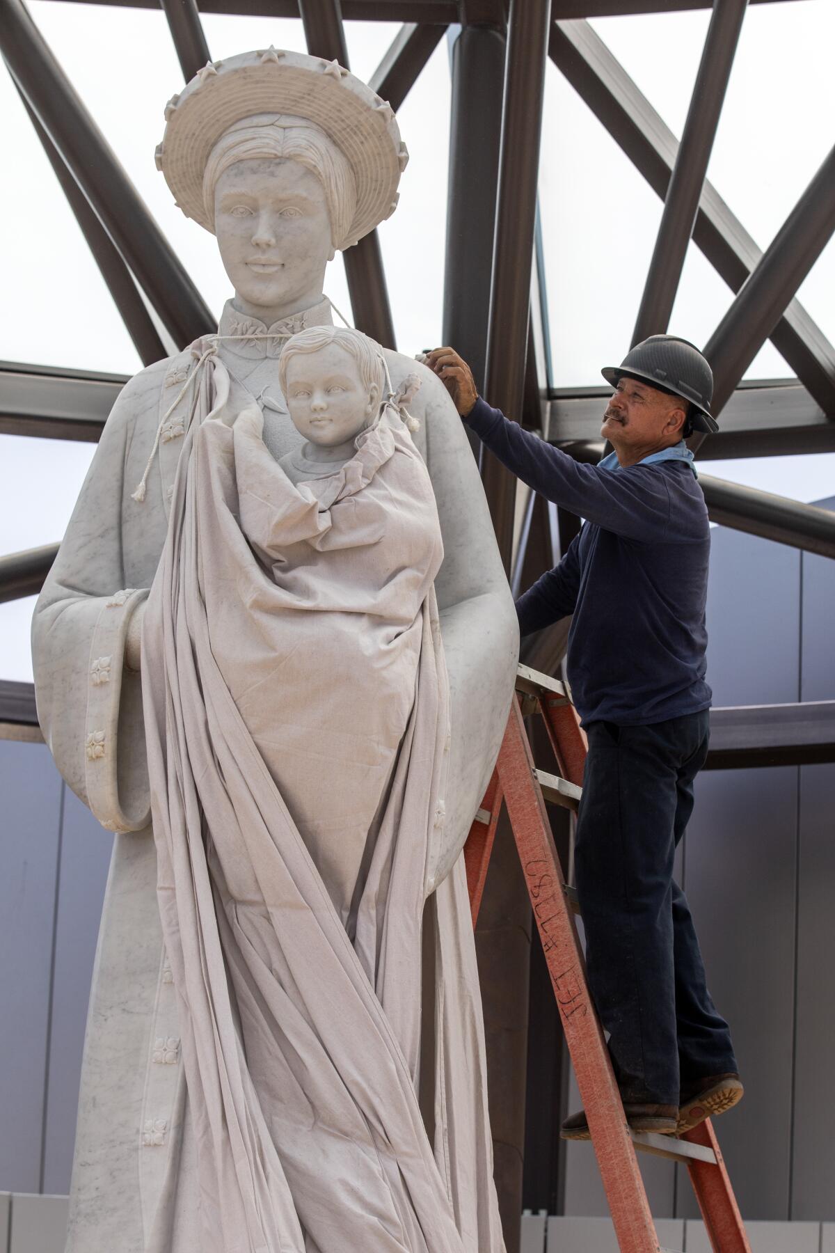 A worker on a ladder unveils a new statue