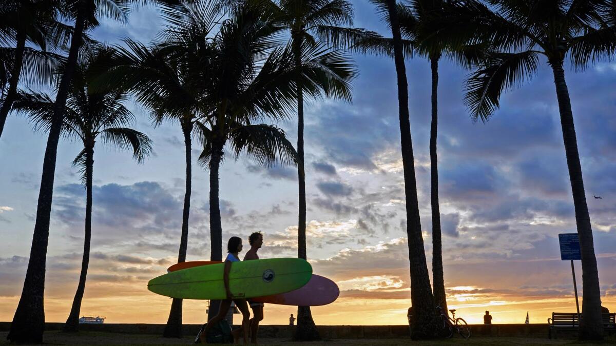 Surfers walk on a sidewalk along Waikiki Beach prior to the pandemic. 