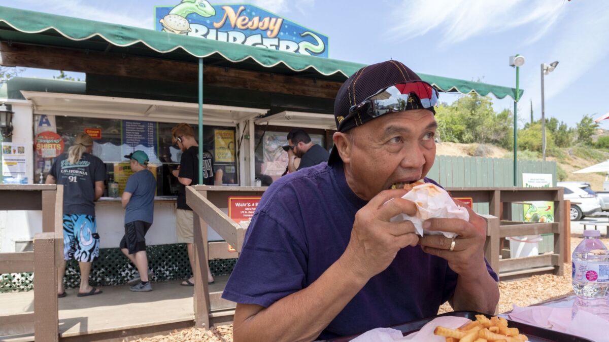 Sam Ordinary, a longtime customer of Nessy Burgers in Fallbrook, digs into one of the roadside stand's half-pound Nessy Burgers on Tuesday. The trailer-based eatery will soon move into a permanent restaurant space next door.