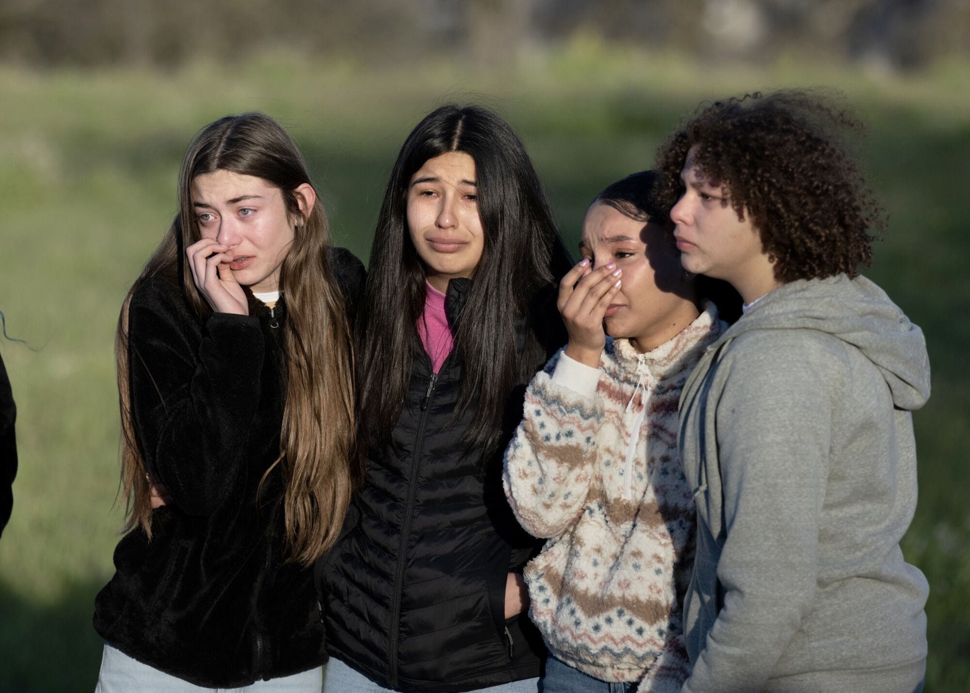 Four teen girls embrace one another while grieving during a memorial service.