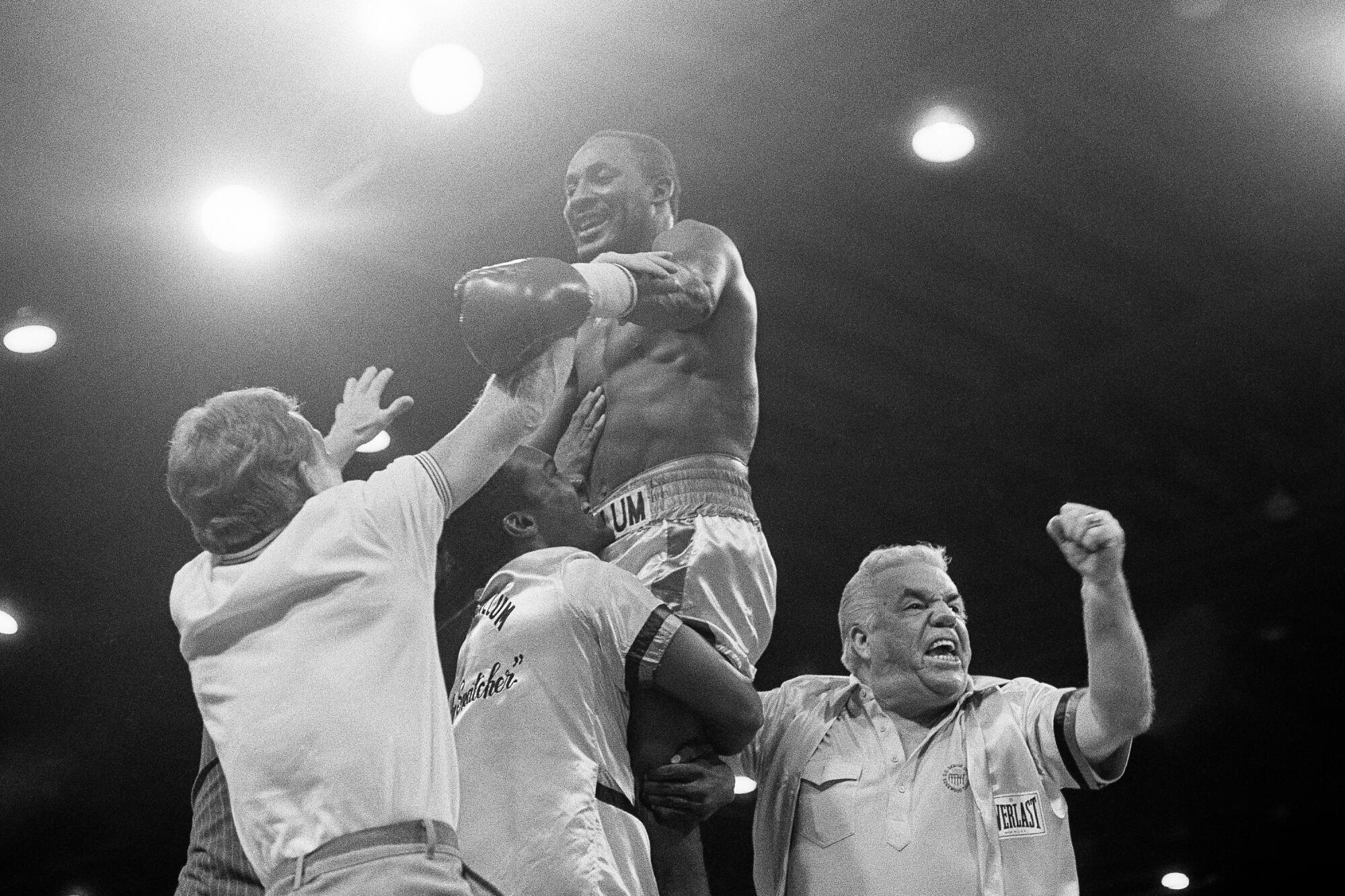 Mike McCallum wears boxing gloves and is lifted up by one man while three others surround him
