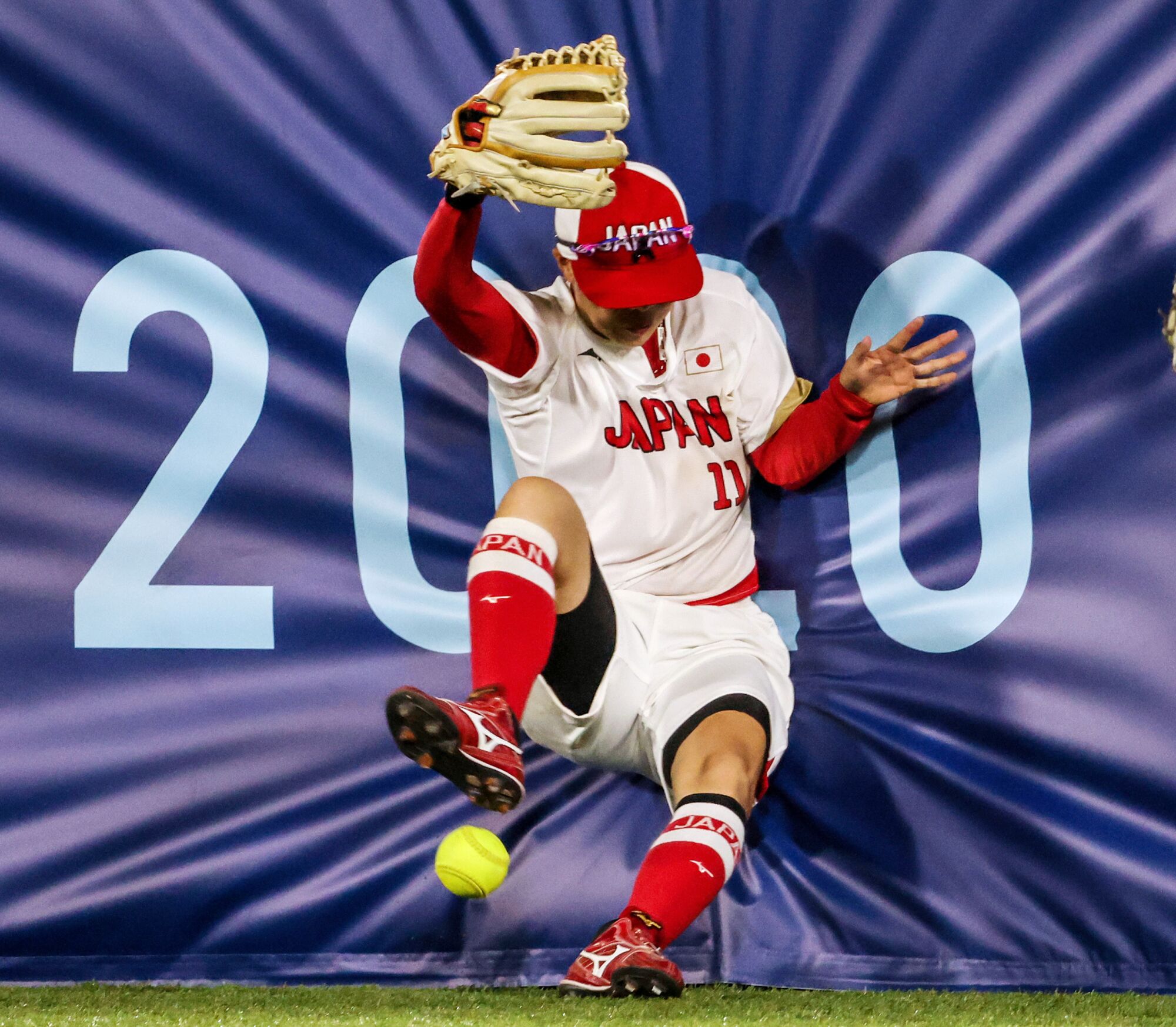 A player falls into padding on a fence, the softball near her feet.