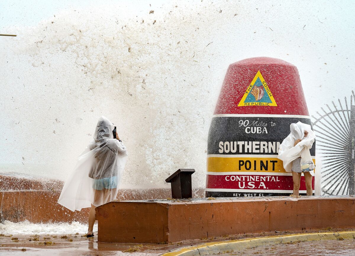 Visitors to the Southernmost Point buoy in Key West, Fla., brave the waves for photos as the island chain is under a tropical storm warning on Friday, June, 3, 2022. Tropical storm warnings were issued early Friday for much of the Florida peninsula, Cuba and the Bahamas as a system that battered Mexico moves through the Gulf of Mexico, bringing threats of heavy rain and wind for the weekend. (Rob O'Neal/The Key West Citizen via AP)