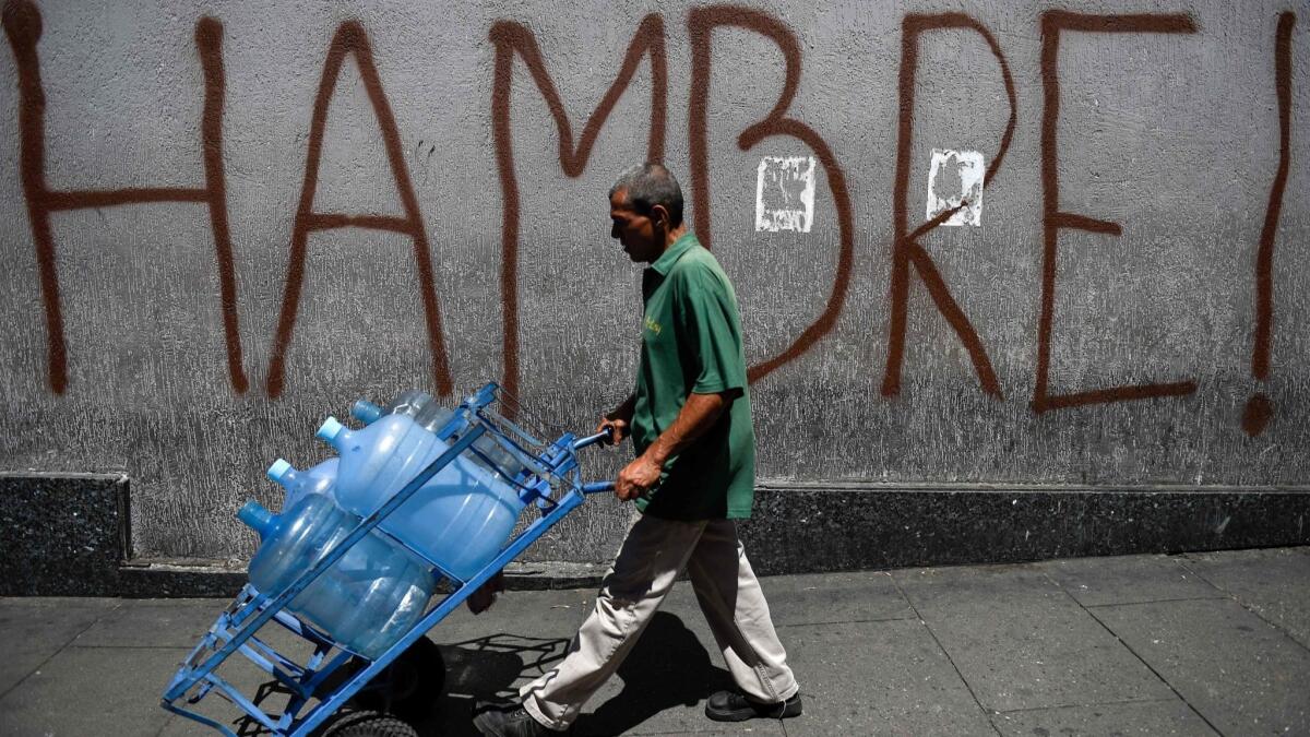 A man pushes a cart past graffiti reading "Hunger" in Caracas, Venezuela.