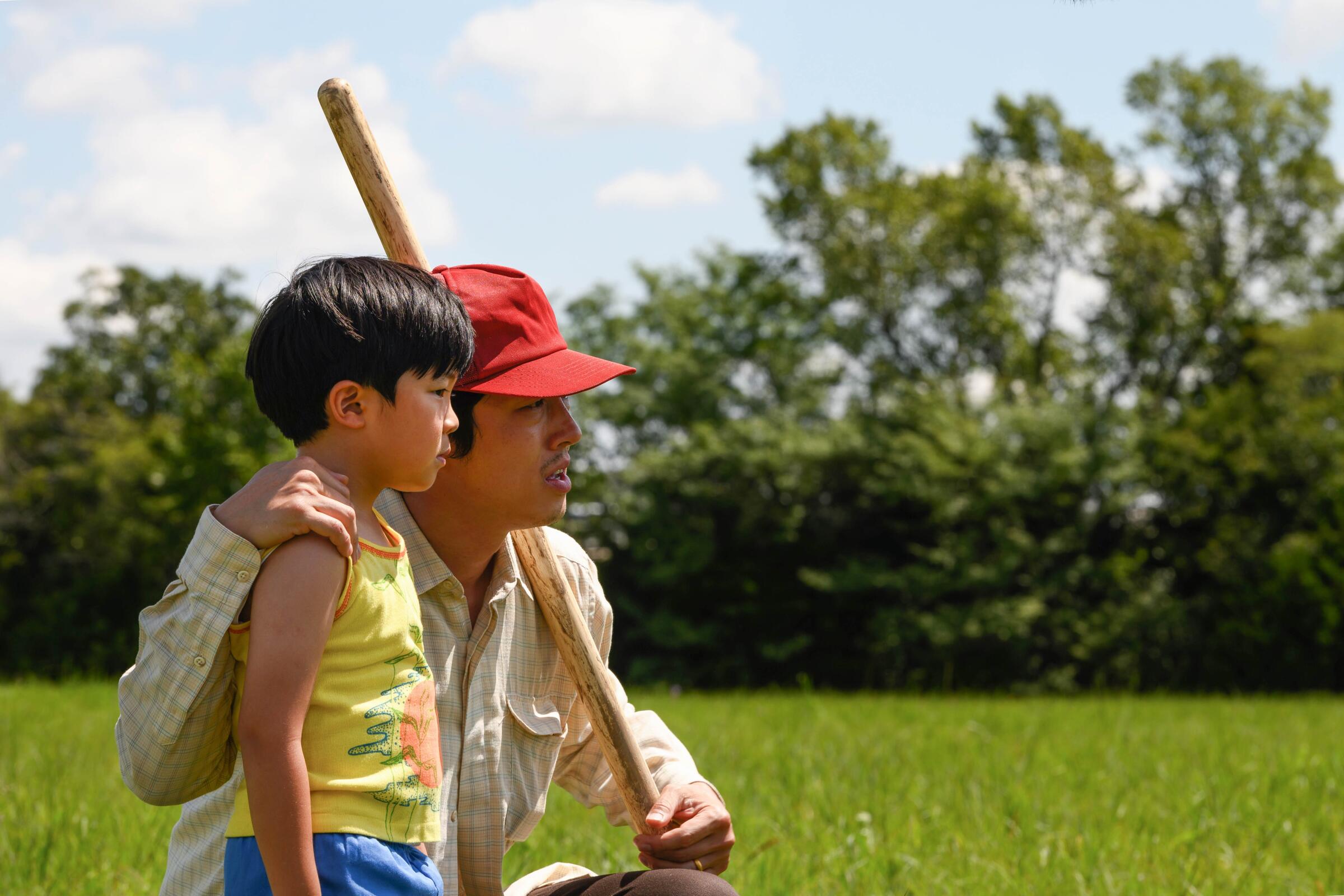 Steven Yeun, in a red hat holding a baseball bat, with Alan Kim in "Minari"