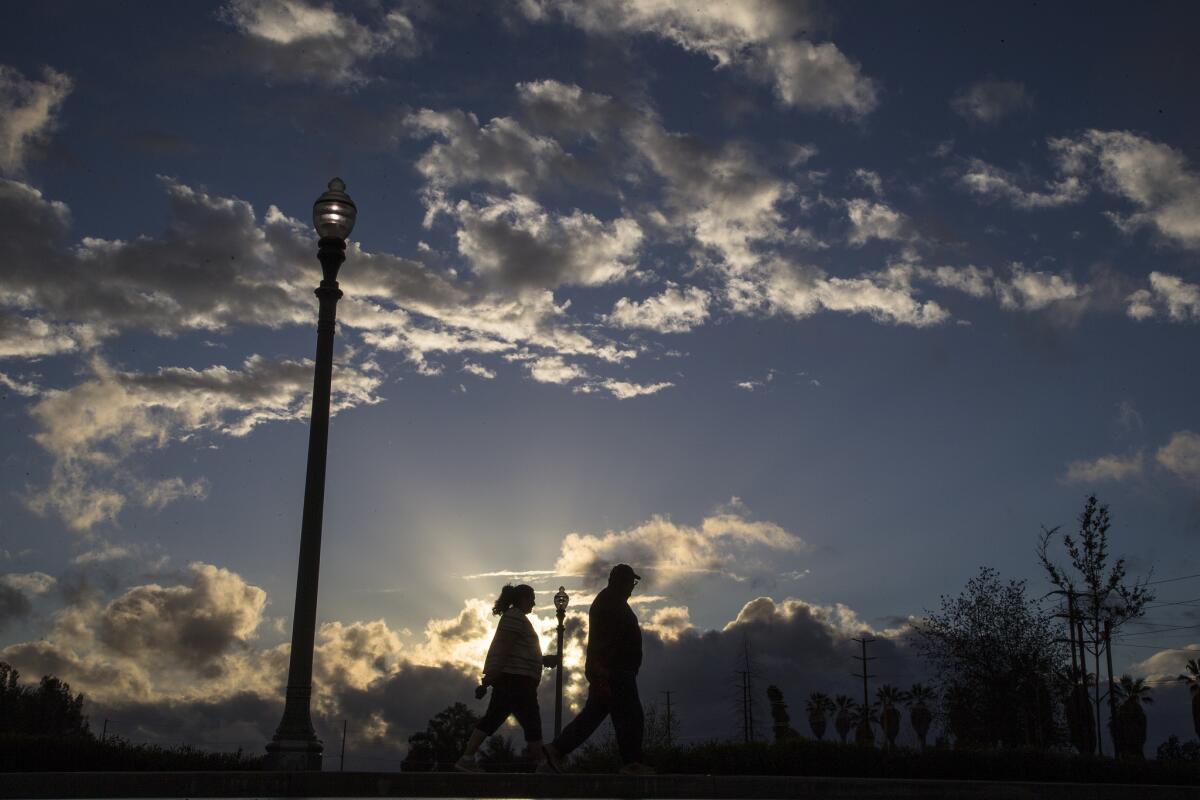 Storm clouds clear enough to allow the setting sun to peak through as a couple enjoys a stroll in Ryan Bonaminio Park on March 11, 2016, in Riverside. Rain may make an appearance, along with cooler weather, in Southern California this week.