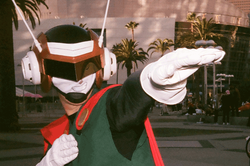 A gif of a person wearing white gloves, a green and red tunic and a helmet with antennae