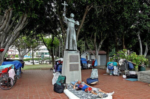 A homeless man sleeps beneath a statue of Junipero Serra at Father Serra Park.